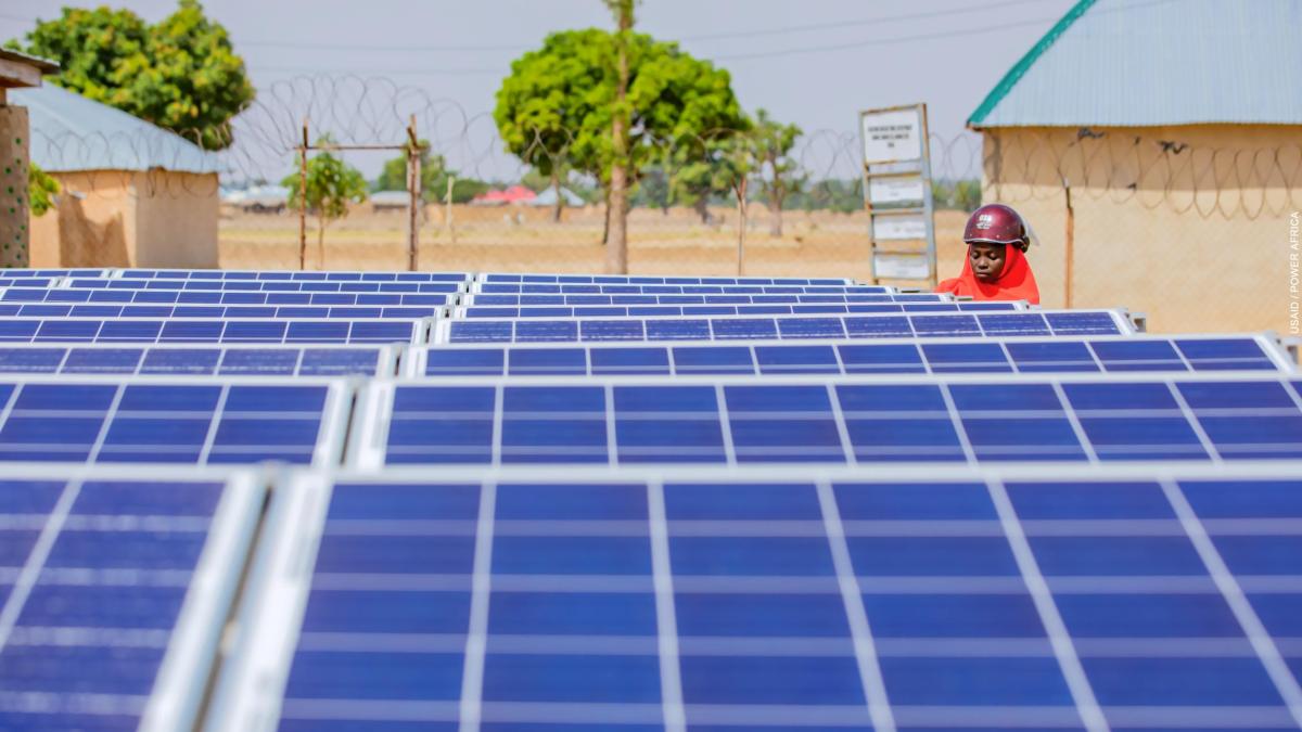 A female Nigerian solar technician inspects a photovoltaic array in a rural community