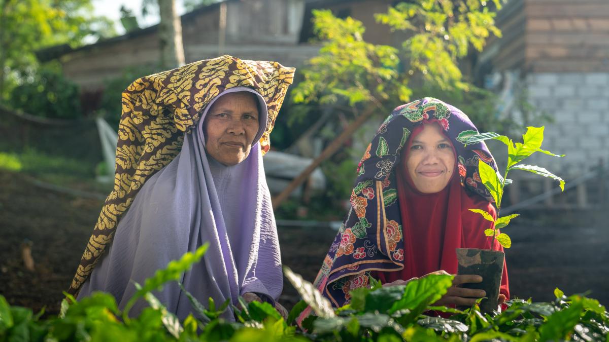 Two women farmers stand in front of their coffee plants.