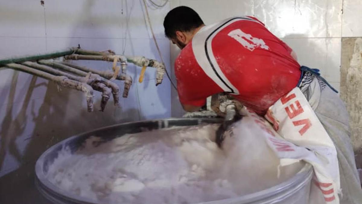 A bakery employee toggles the controls on the dough mixer to produce a fresh batch of goods. 