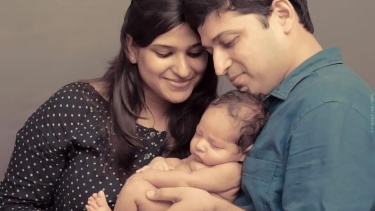 Portrait of a modern Indian family. A young mother and father smile on their infant they are holding.