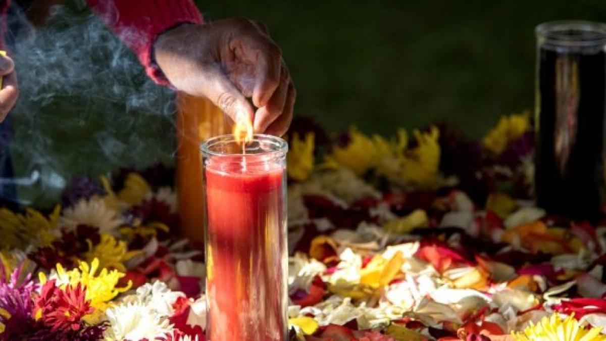 Indigenous A hand lighting a red candle surrounded by white, yellow, and red flowers in a dark room.Women Authority leading the beginning of a meeting in Huehuetenango in 2019