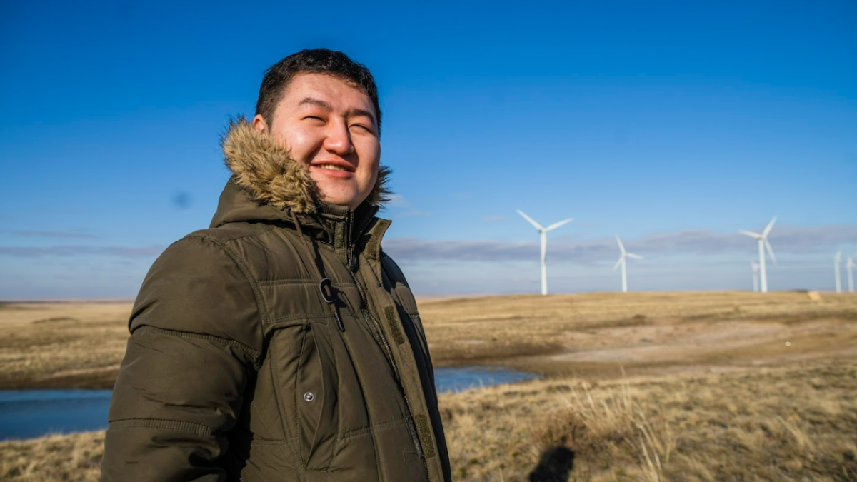 A man poses in a field in front of windmills.