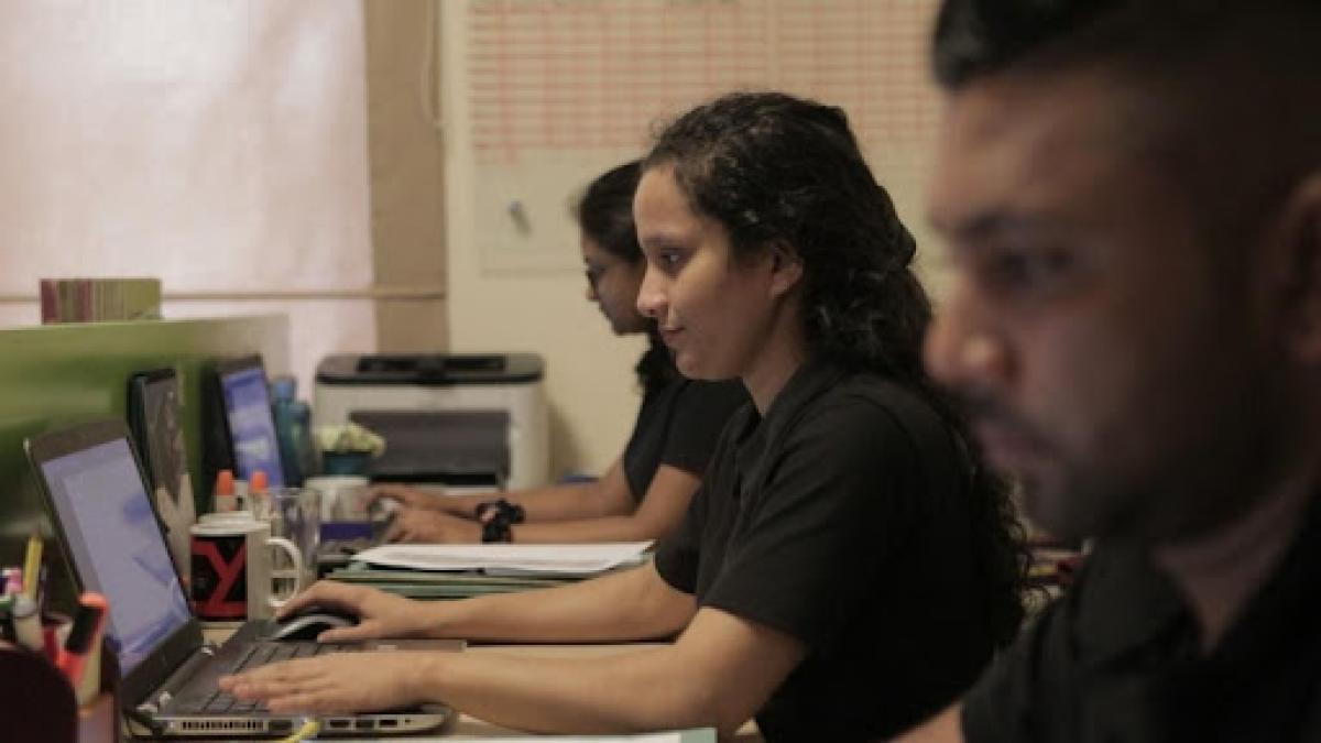 Woman working on laptop computer alongside two other people. 