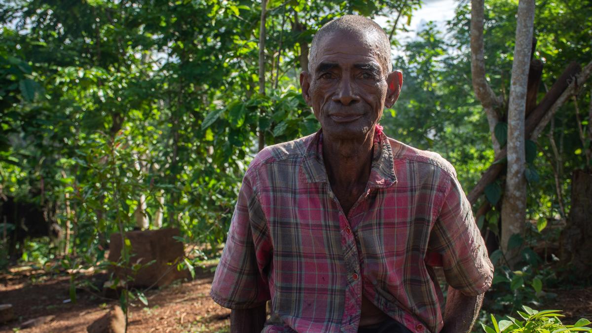 A farmer from Madagascar smiles, with a forested area in the background