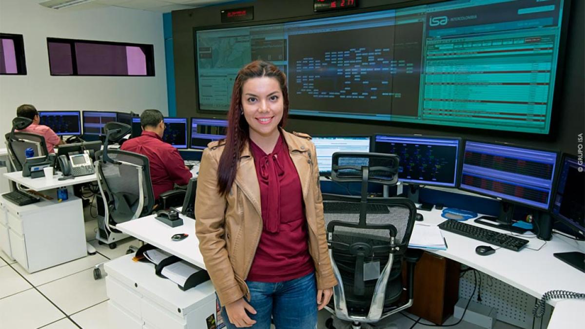 A smiling woman stands near her computer station in a high-tech network operation control room