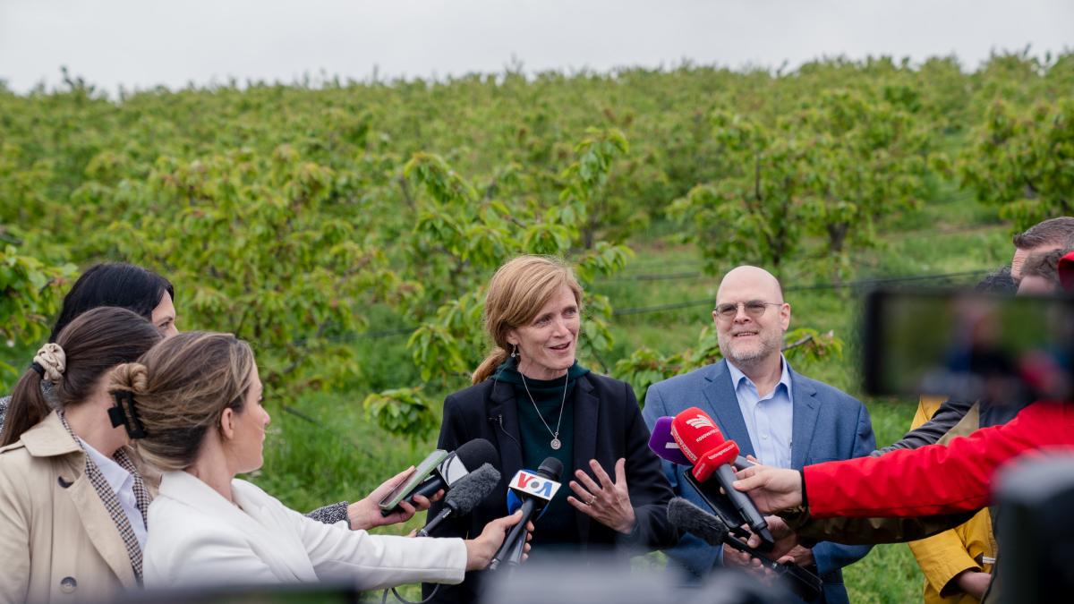 Administrator Power participates in a press gaggle in front of an orchard with lush trees