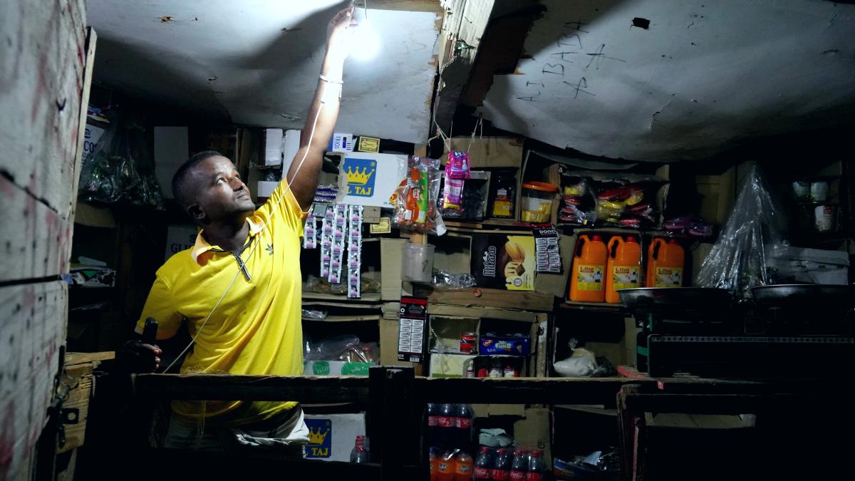 A shopkeeper lights his lamp to illuminate his shop utilizing mobile solar batteries. Kalaf Village, Djibouti.