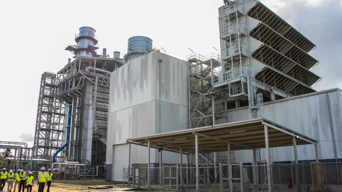 A group of people wearing safety gear walking on the construction site of of a natural gas power plant.