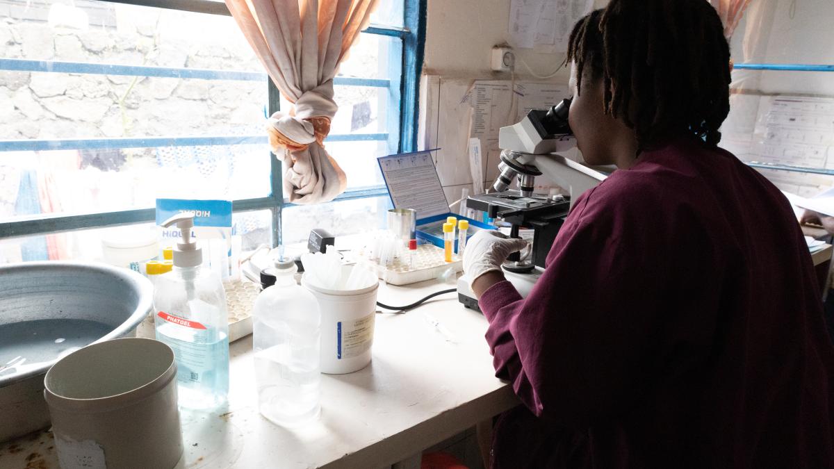 A lab technician in a community clinic inspects a patient’s culture for signs of infection.