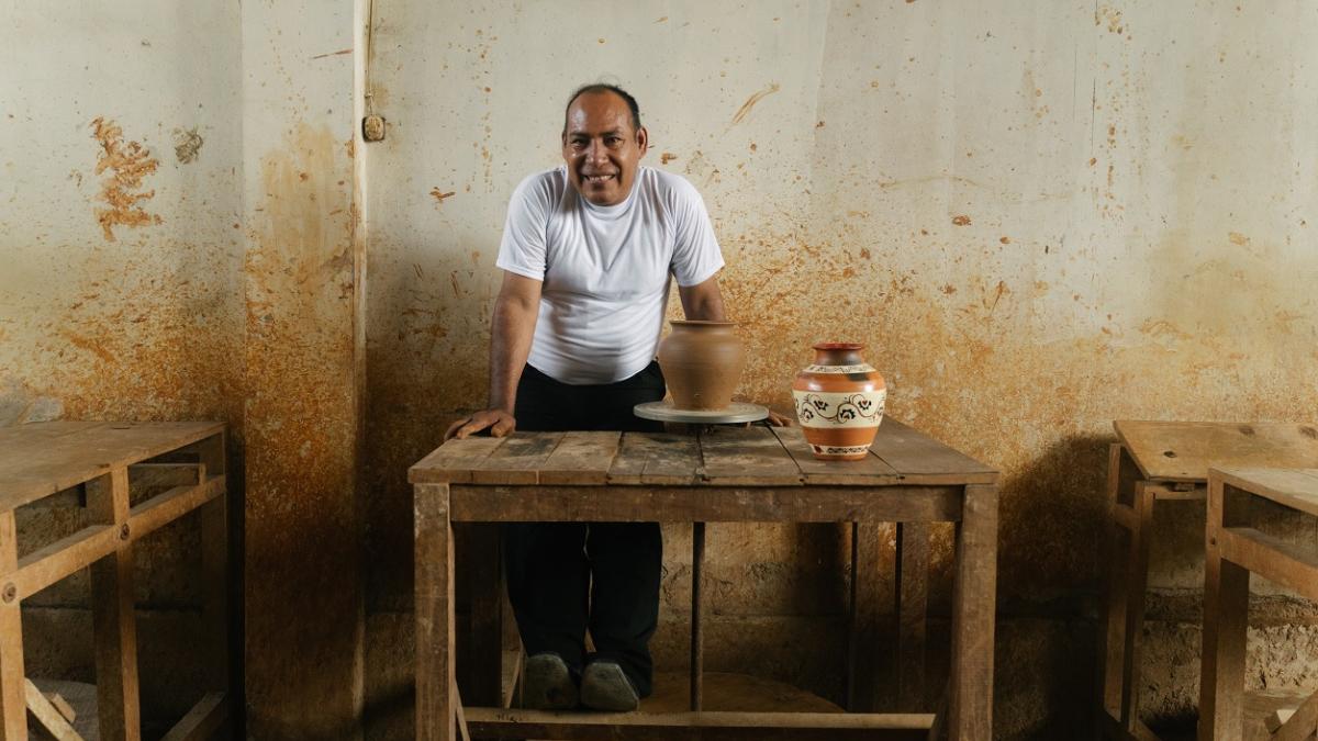 A man smiles beside two vases in a pottery studio.