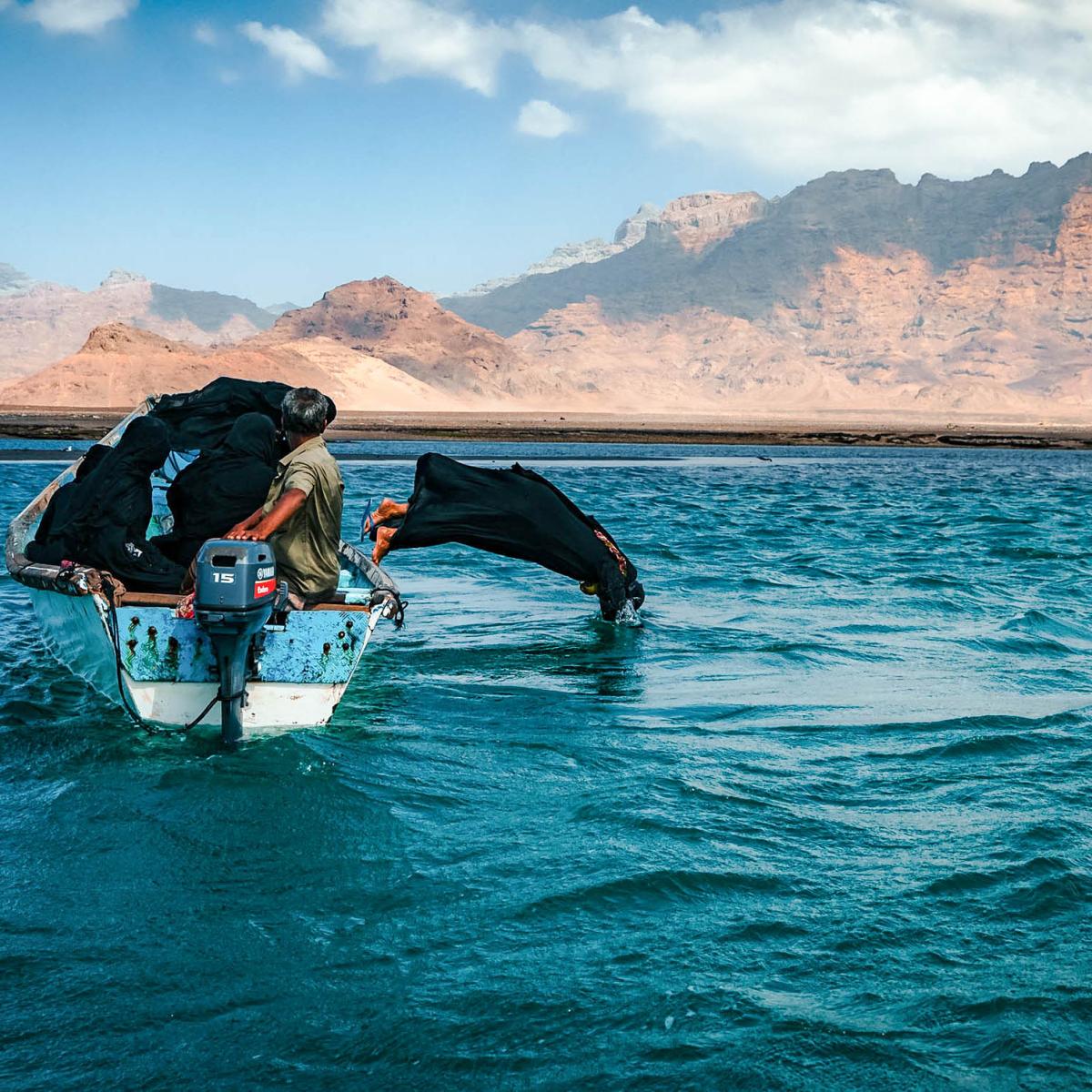 Woman jumping off of a boat into the water with mountains in the background