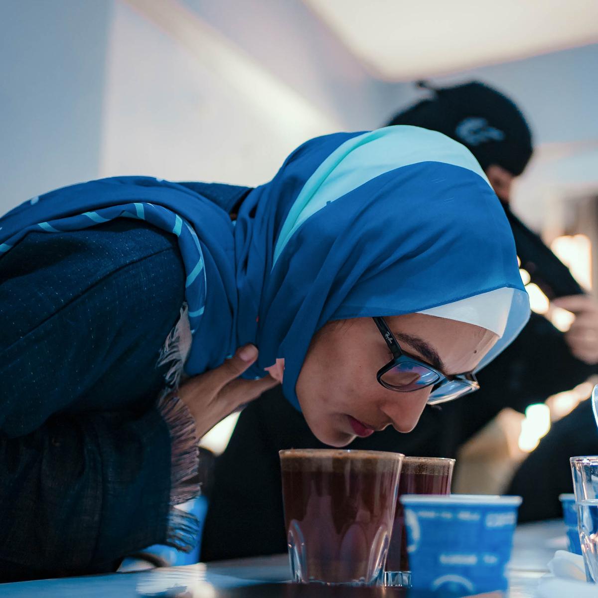 Woman attending a coffee training is leaning over to smell a cup a coffee sitting on a table