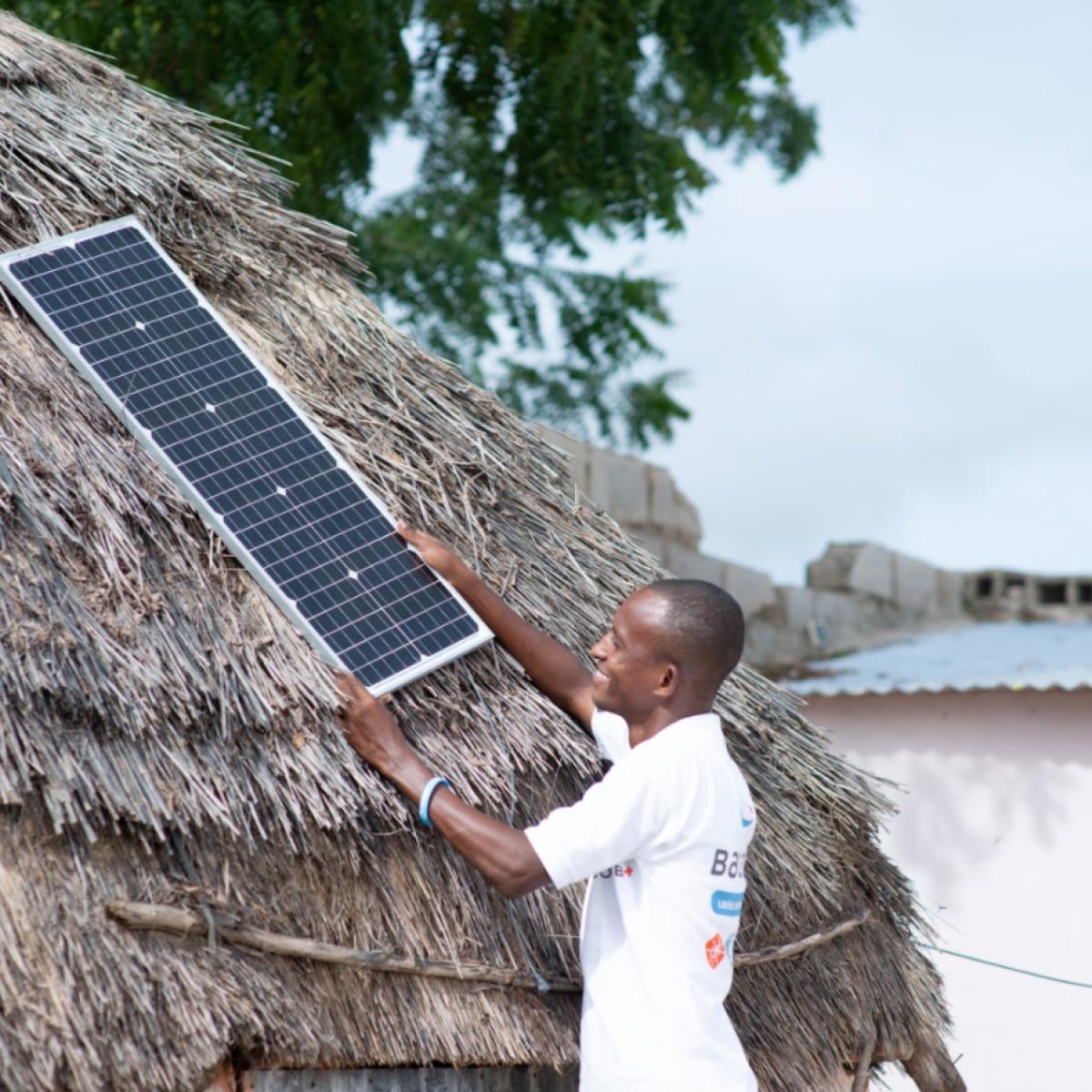 Un agent de Baobab Plus pose un panneau solaire sur une maison