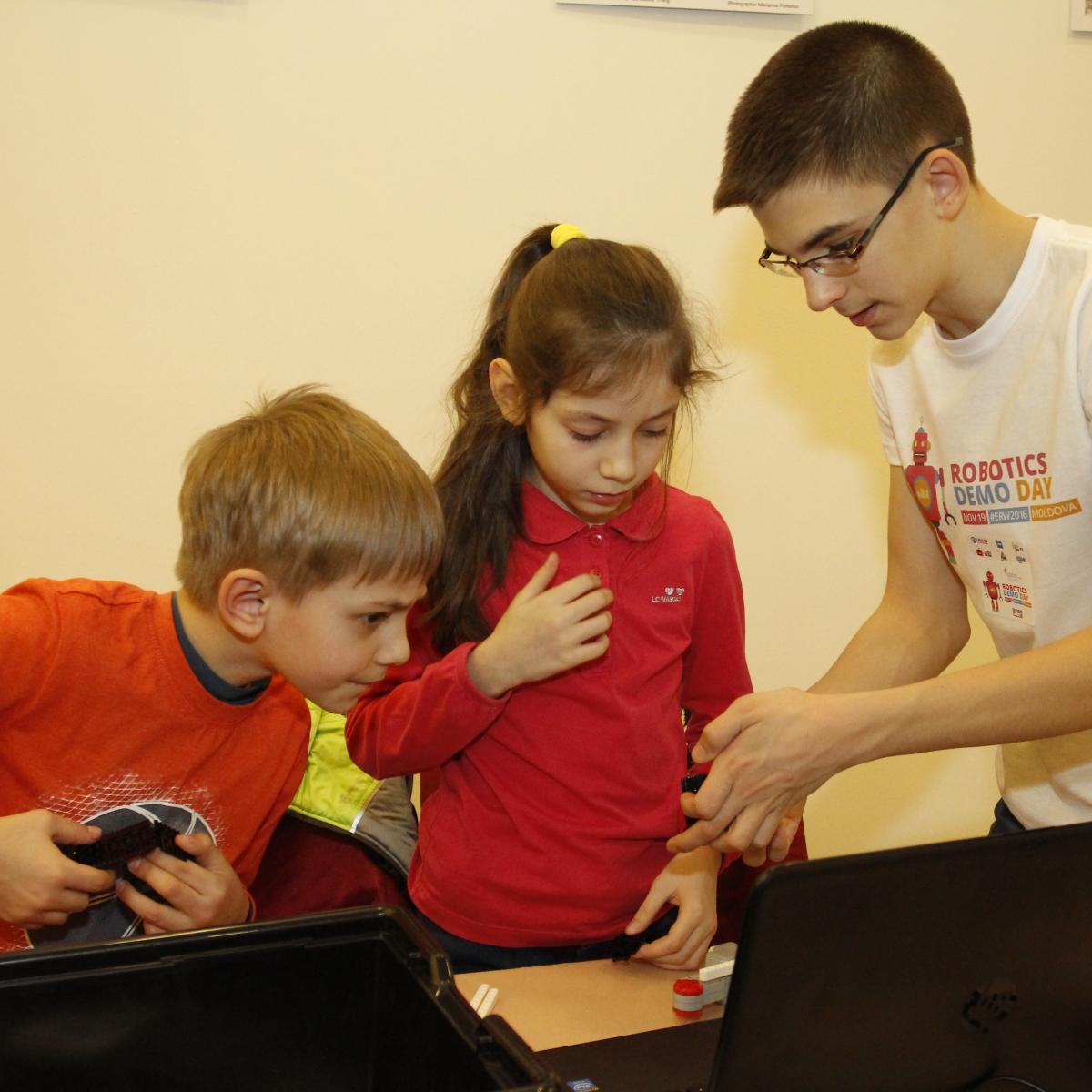 Andrei Copaci îndrumă doi copii în procesul de construire a unui robot, în cadrul EU Robotics Demo Day 