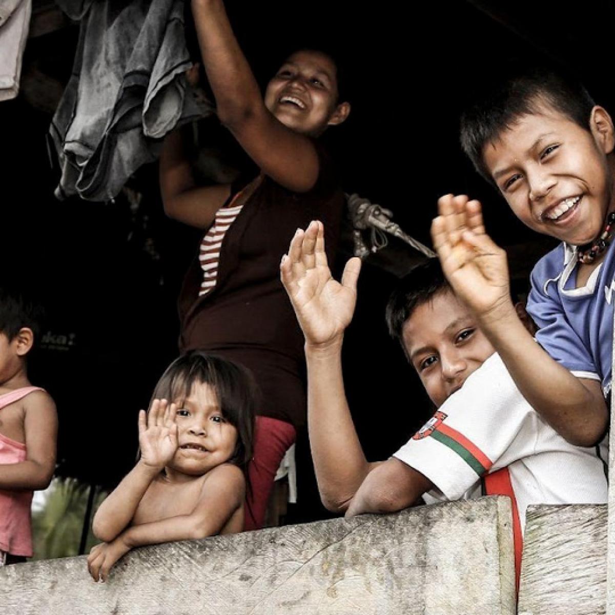 Un grupo de niños y niñas saludando y riendo dentro de una casa en la Amazonía