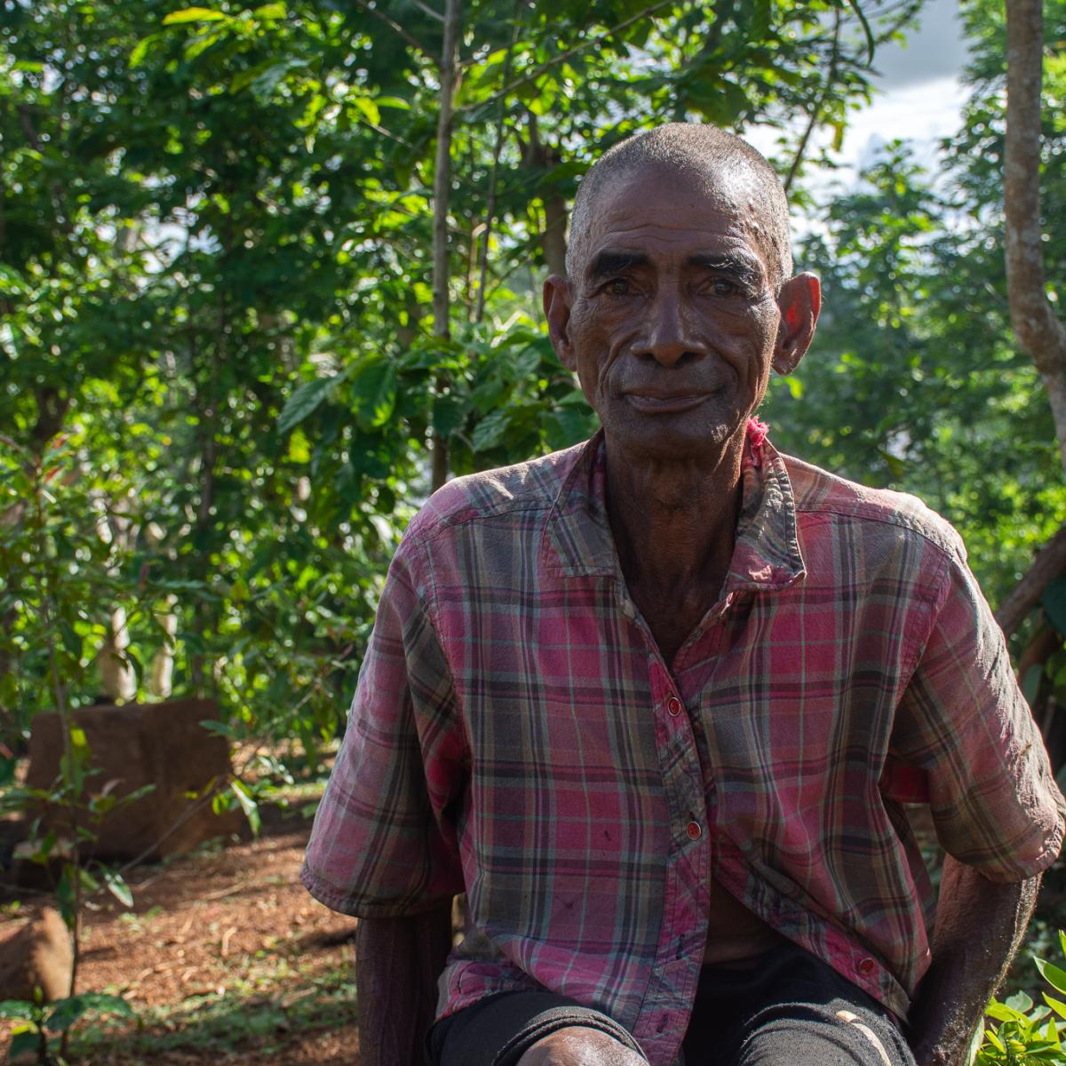 A farmer from Madagascar smiles, with a forested area in the background