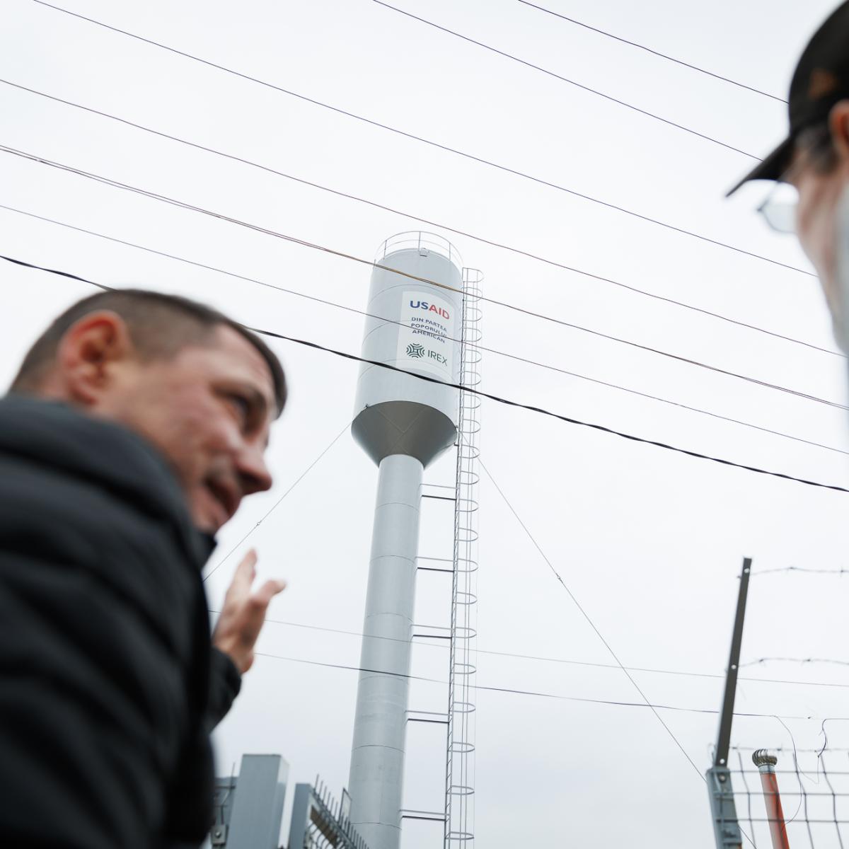 Two men watching a new water tower with USAID logo