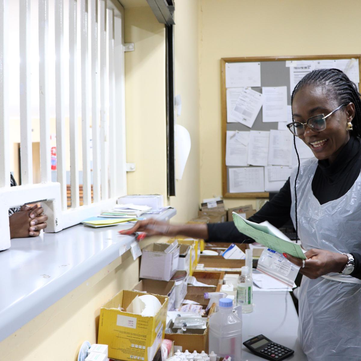 Anna Naukushu dispensing medication to a client at the pharmacy.