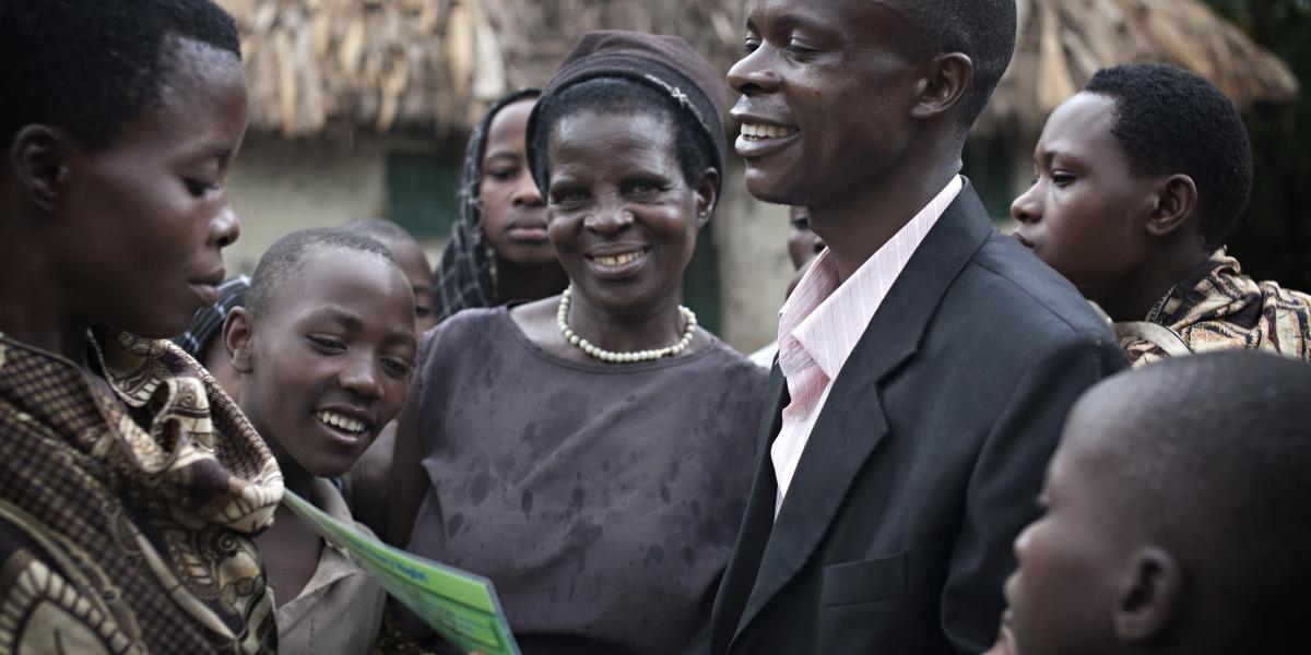 A group of health cooperative members in Uganda smile, looking towards a piece of paper held by a man in the middle.