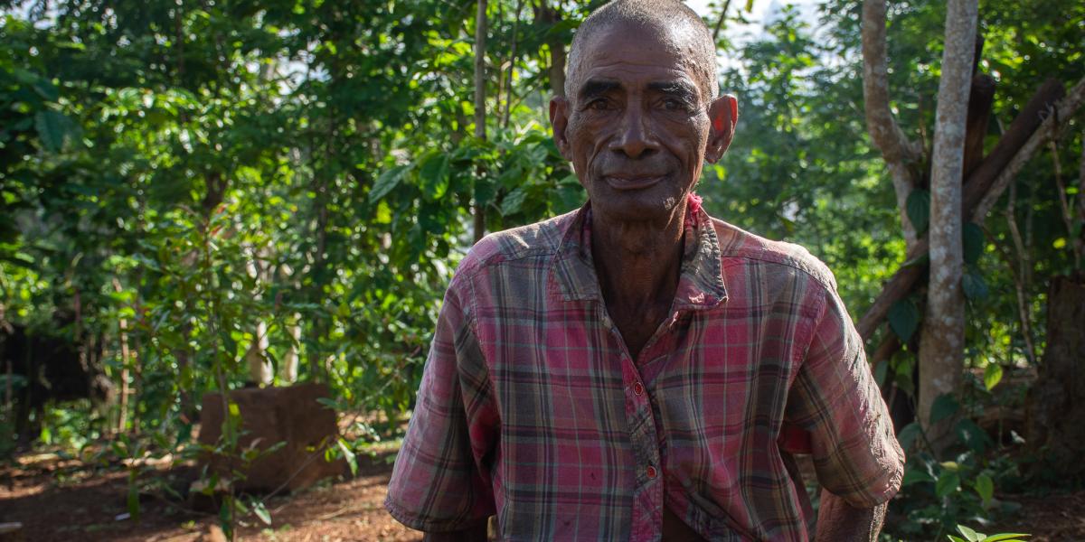 A farmer from Madagascar smiles, with a forested area in the background