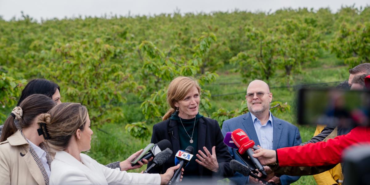 Administrator Power participates in a press gaggle in front of an orchard with lush trees