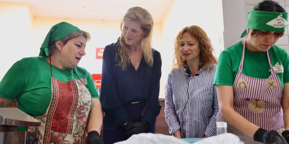 four women stand in a row and speak while making food