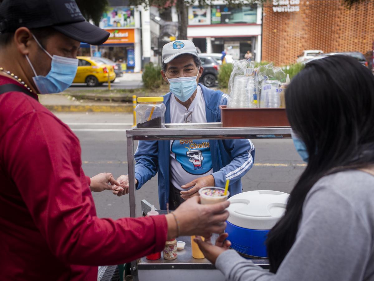 This picture shows Carlos Torres selling his product, chicha, to two people. 