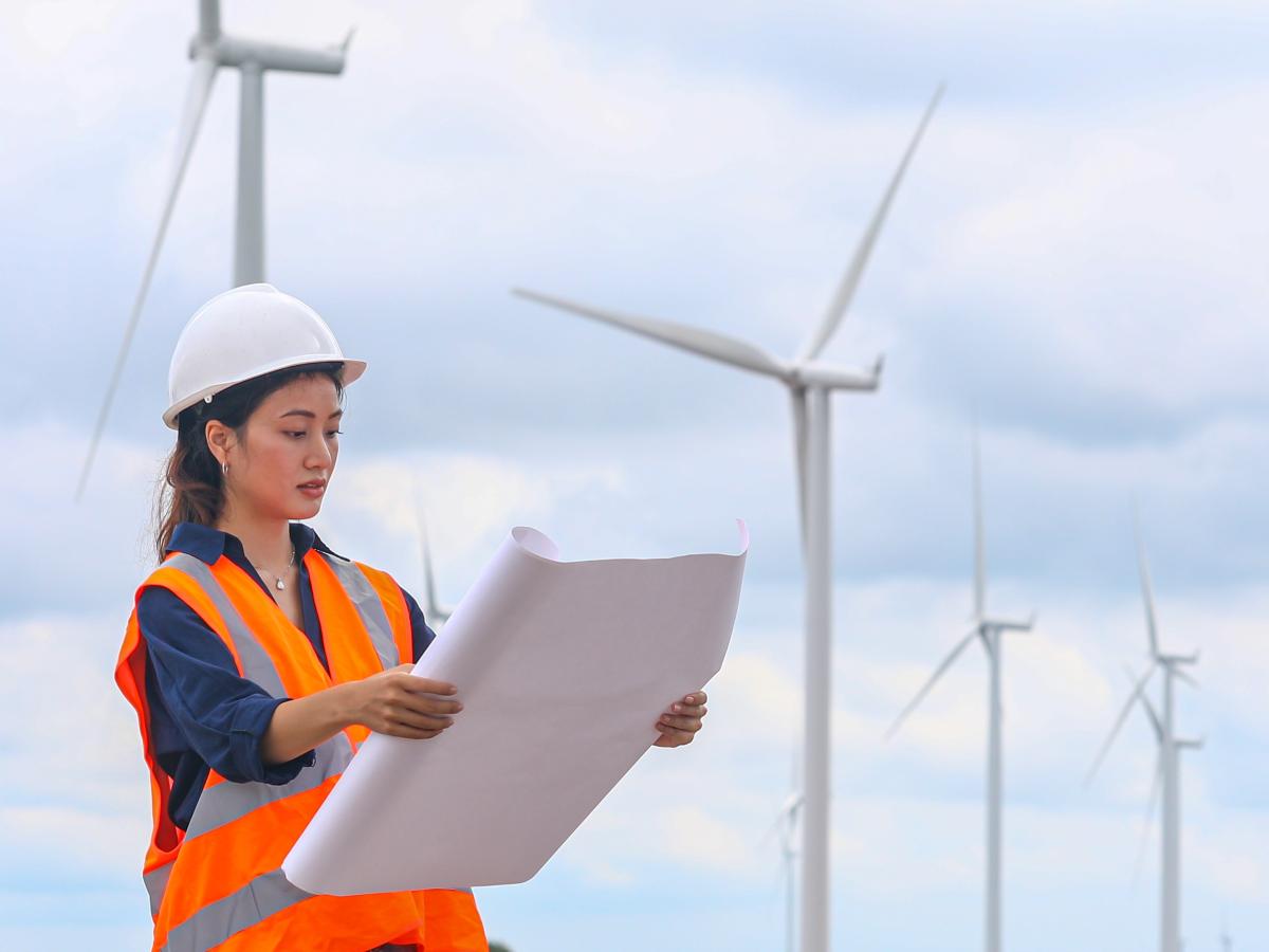 A female engineer examines planning documents while working at a wind-powered clean energy plant.