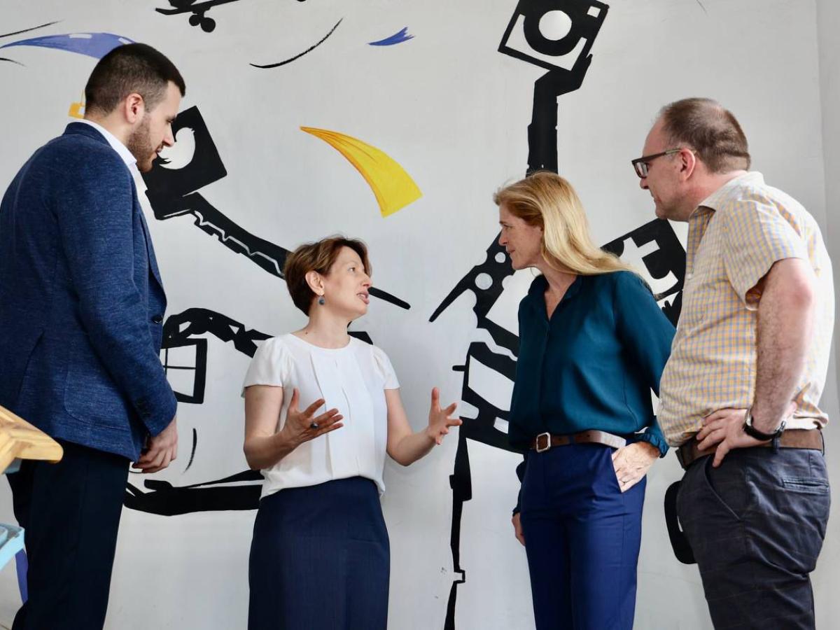 four people chat in front of a mural