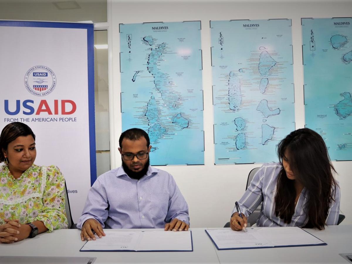 Two people at a table sign documents while a third person looks on.