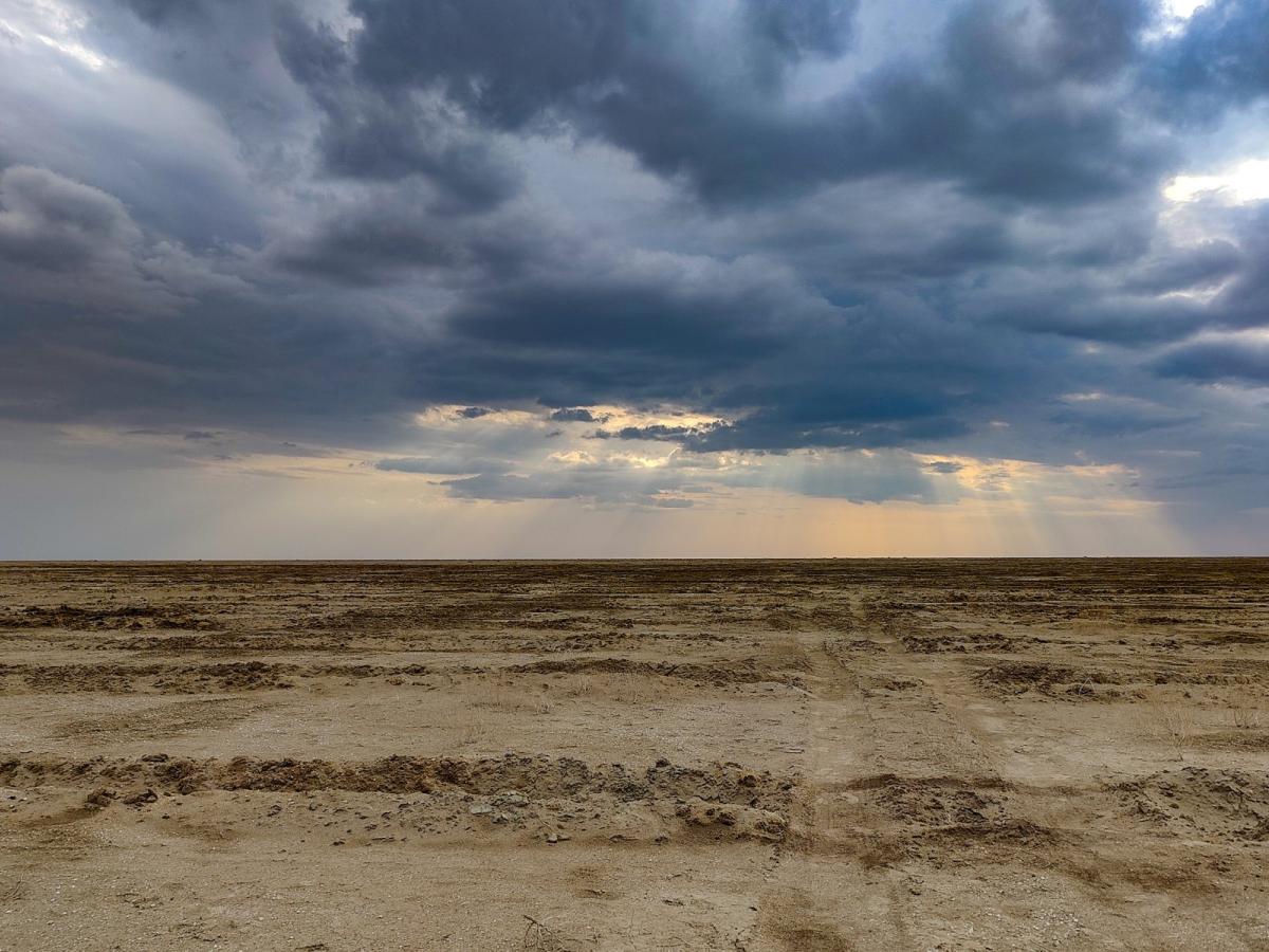 The sun shines through dark blue clouds over a dry, deserted area