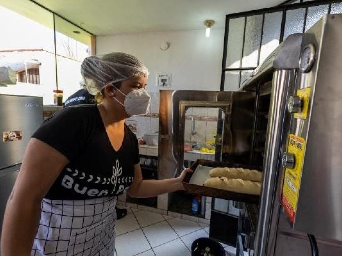 Adriana holding a plate, placing the loaves in the oven.