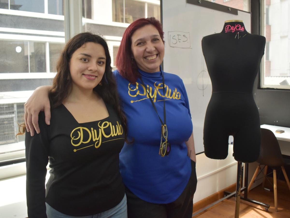 This pictures shows Laura and Dani standing in front of the camera with one arm around each other. They are both wearing shirts that read DIY Club. There is a pinnable mannequin next to them. 