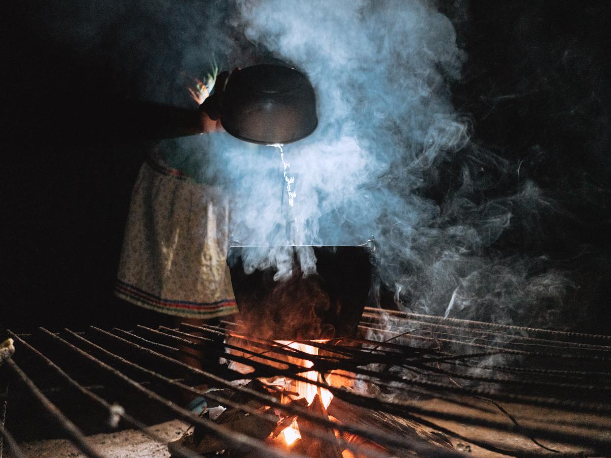 This picture shows a woman pouring a liquid on the pot and steam coming out of it. The room is dark. 