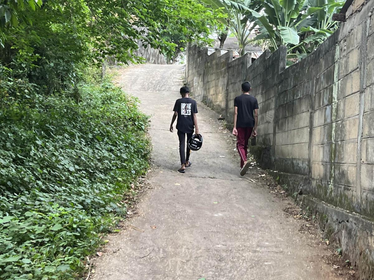 Two boys stroll uphill along a narrow path beside a tall wall.