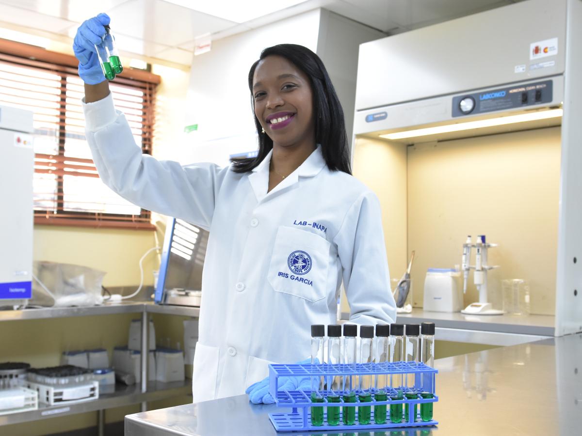 Woman in a lab with a coat is smiling to the camera.