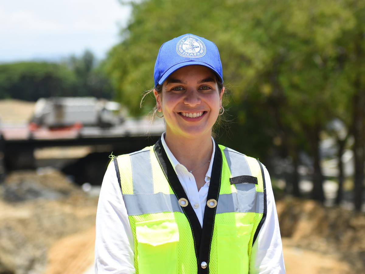 Woman smiles and looks to the camera. She has a cap.