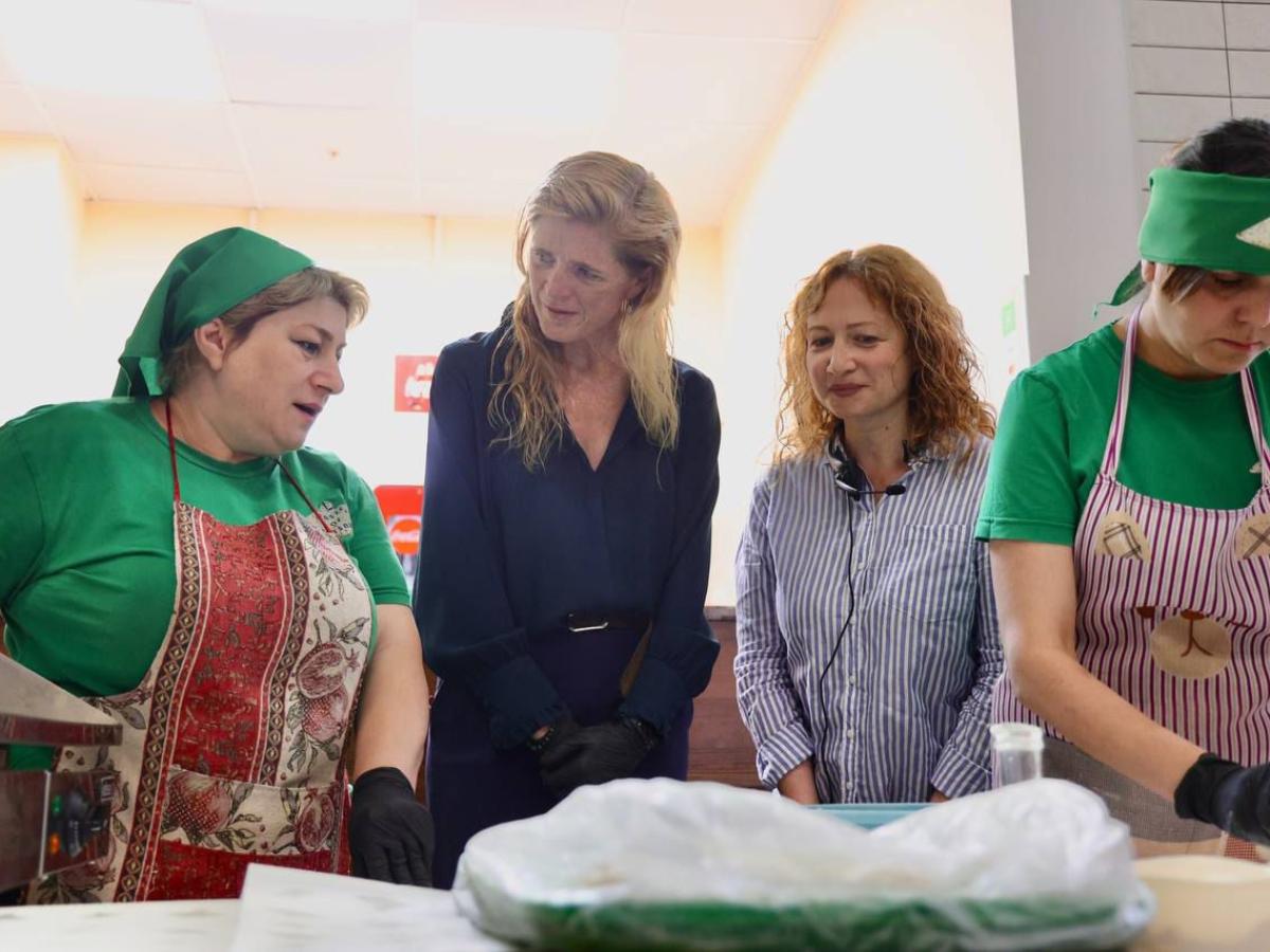 four women stand in a row and speak while making food