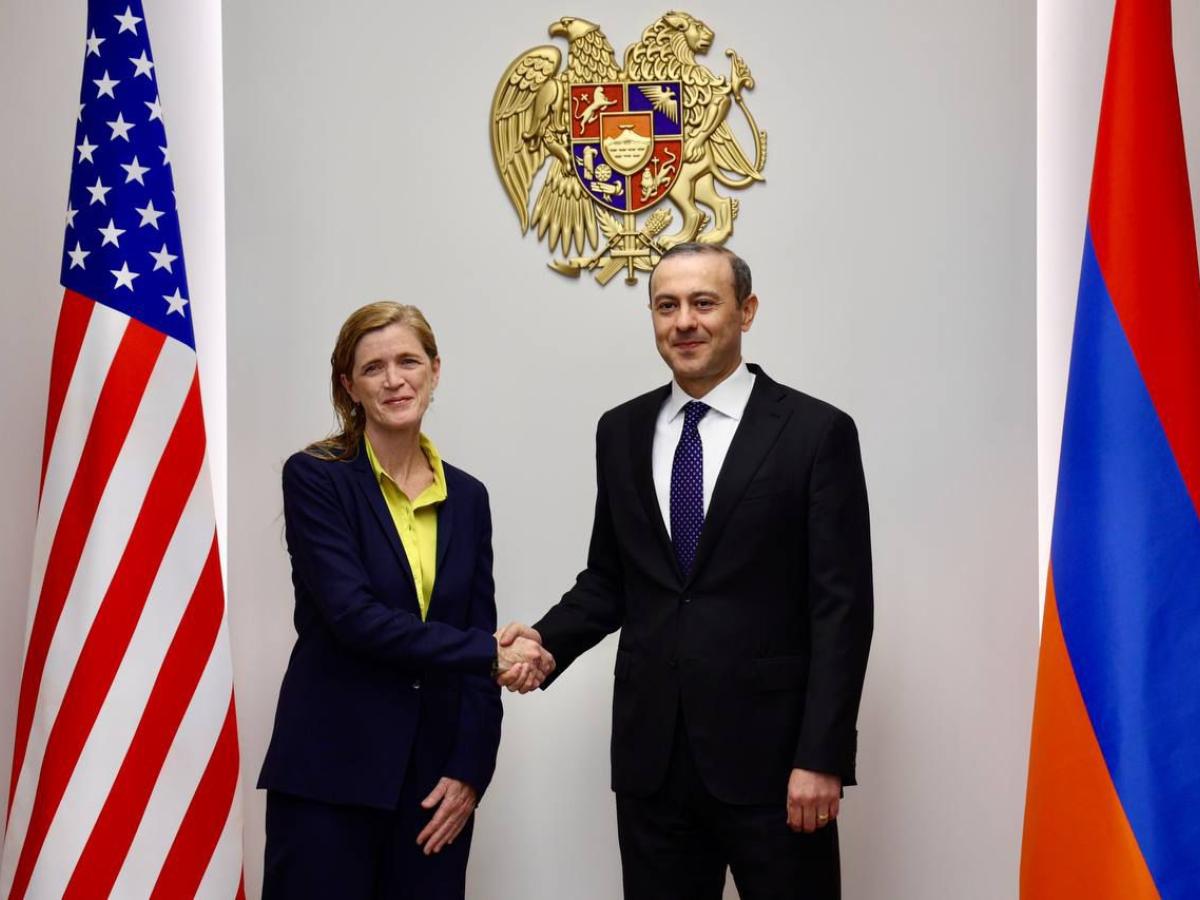 A woman and a man stand in front of U.S. and Armenian flags