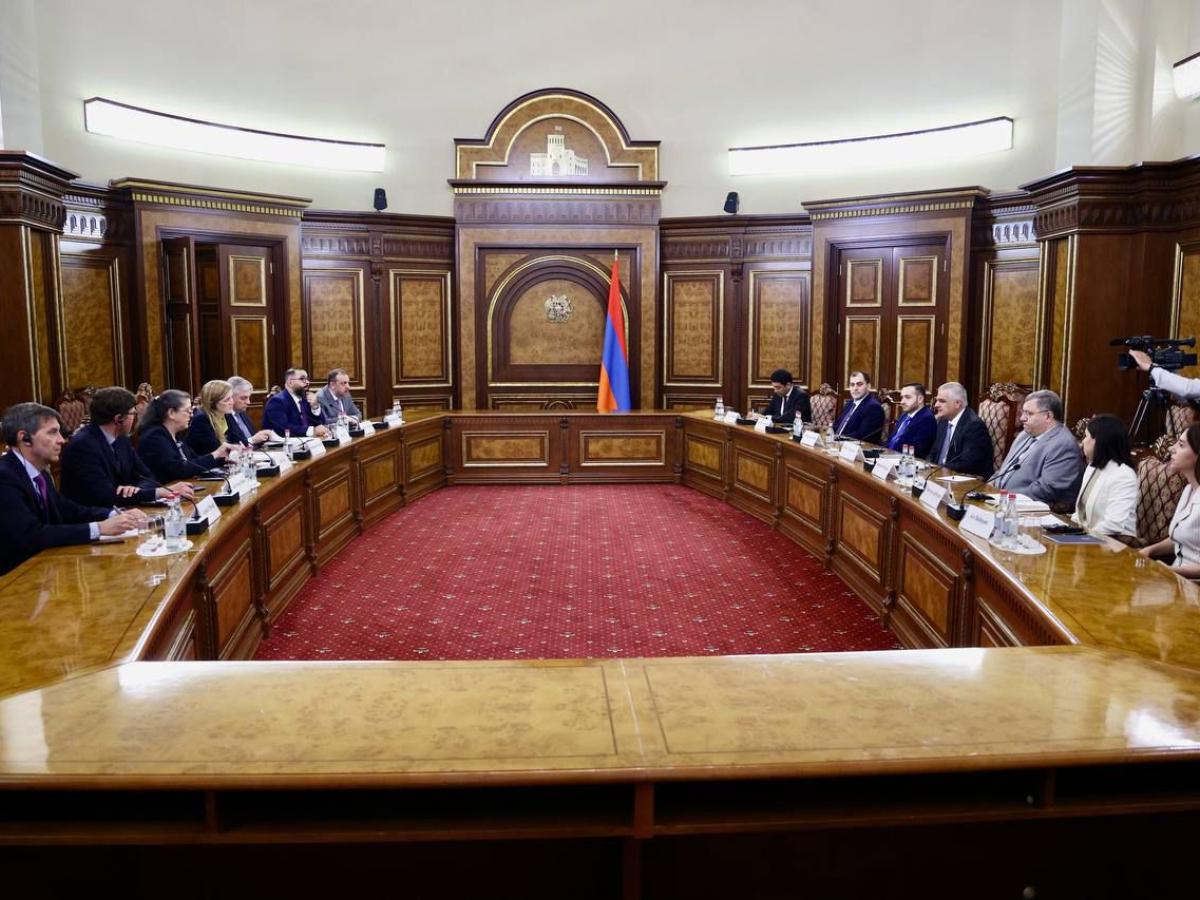 A group of people sit at a formal boardroom table