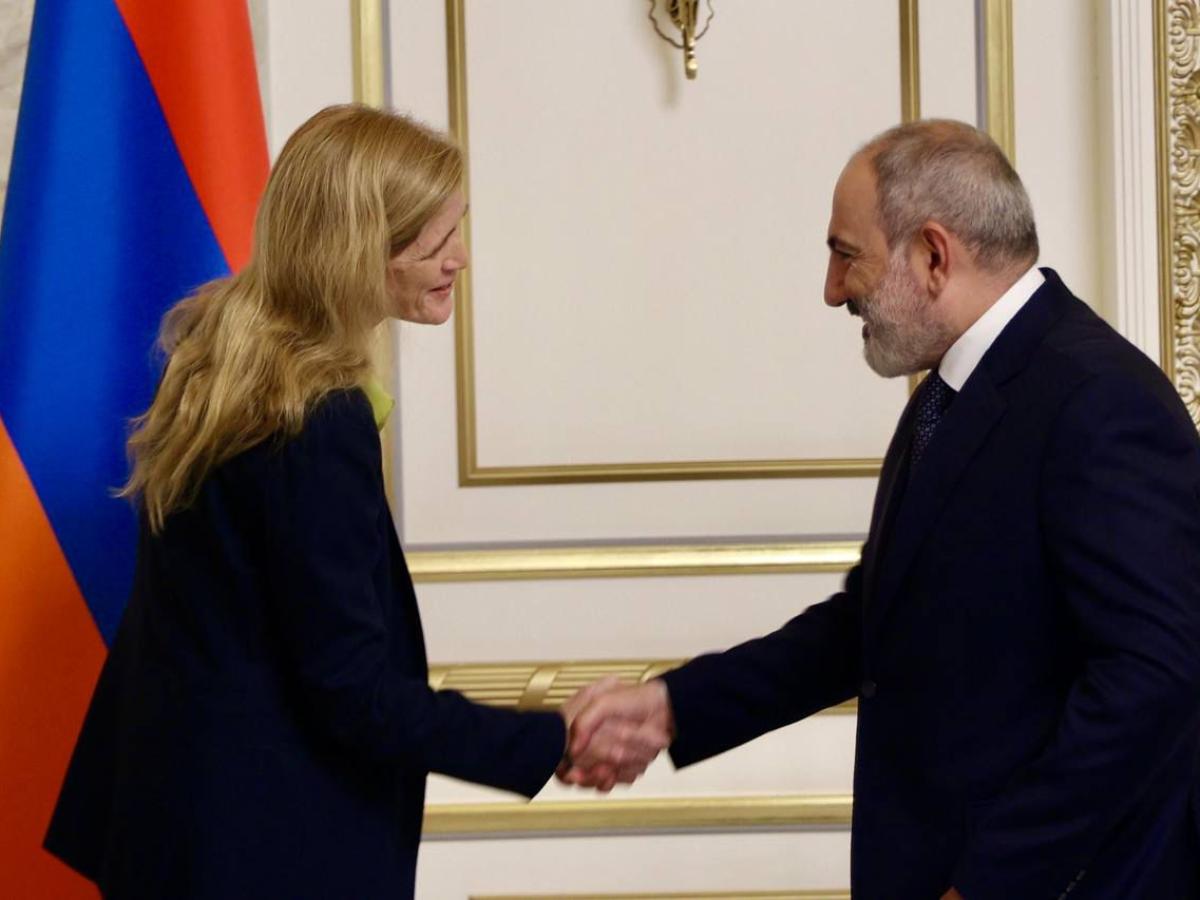 A woman and a man shake hands in front of an Armenian flag