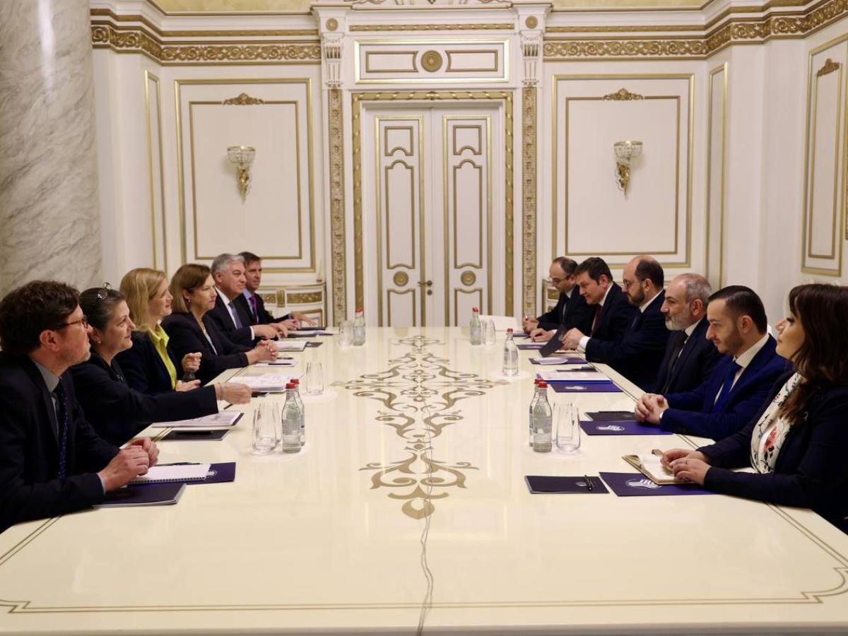 A group of people sit at a formal boardroom table