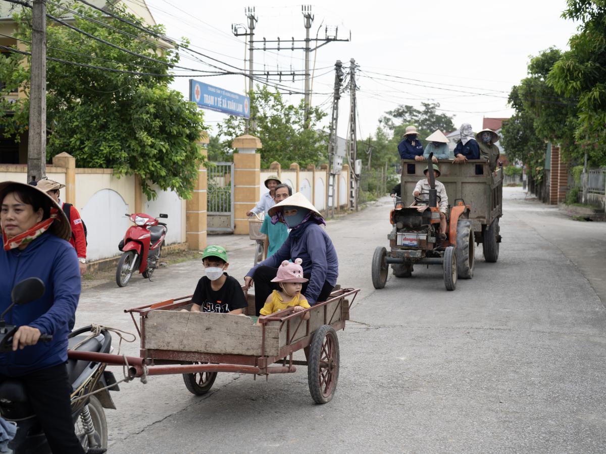 A young man lifts an elderly man’s too-heavy sack of rice; a tractor is converted to carry the young, elderly, and people with disabilities; and a woman stands at a crossroads, confidently directing the movement of hundreds of her fellow citizens. 