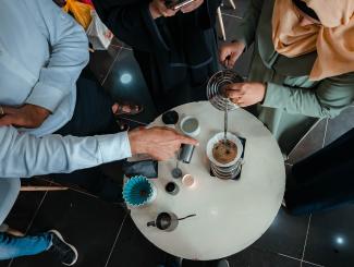 Coffee participants pour water into coffee maker to brew coffee while instructor teaches