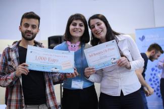 Two young women and a young man hold competition prize certificates for 1,000 euro