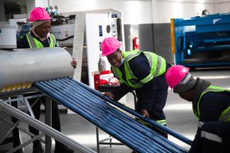 Three learners install evacuated tubes into an evacuated tube solar water heater.