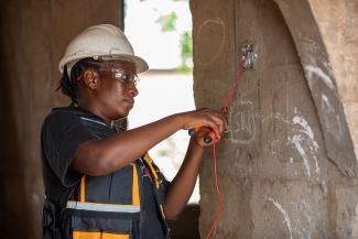 A newly trained electrician wiring a building after she received USAID-supported training and certification.