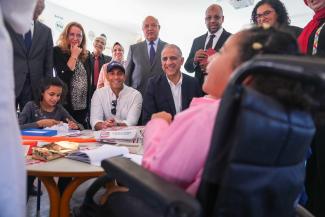 A group of adults in professional dress smile while looking at a child in a wheelchair as she laughs.