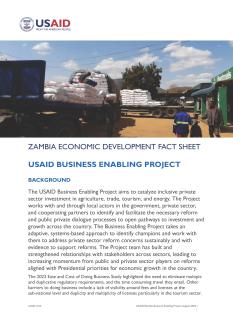 Two Zambian men stand near flatbed trucks loaded with agriculture supplies in this thumbnail for the USAID Business Enabling Project fact sheet