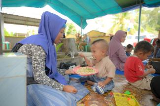 Seorang ibu sedang menyuapi anaknya dengan makanan yang dibuatnya dari bahan-bahan lokal